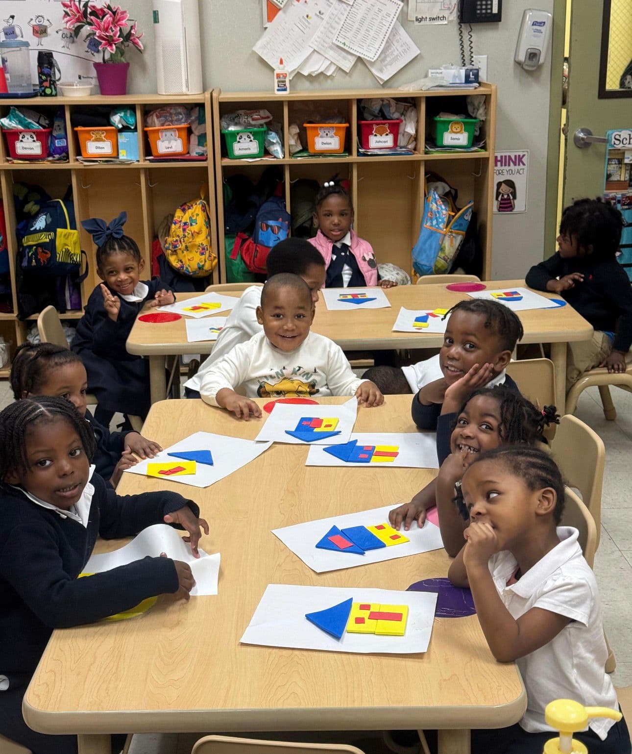 Children smiling while working on a shapes and colors activity at their classroom table
