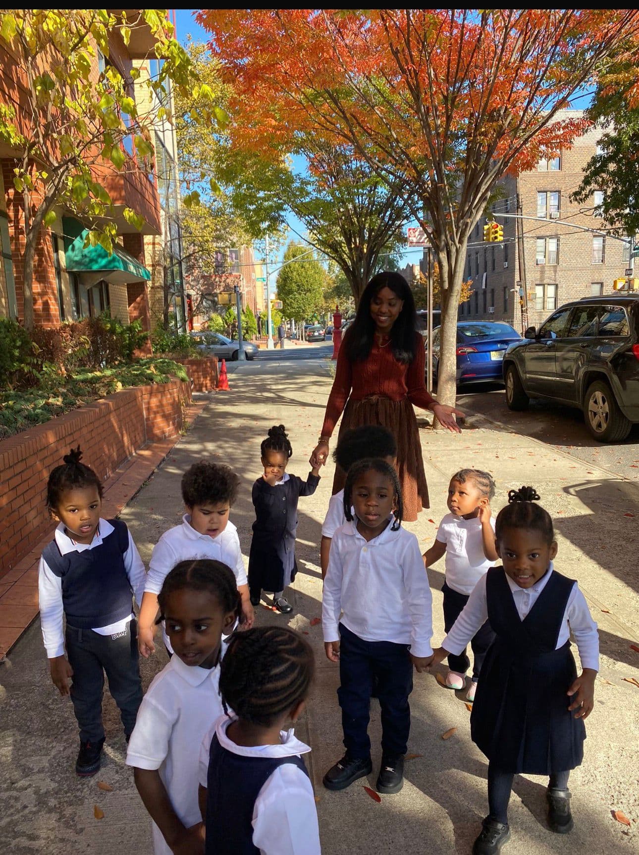 Teacher walking with children in uniforms through the neighborhood on a fall day
