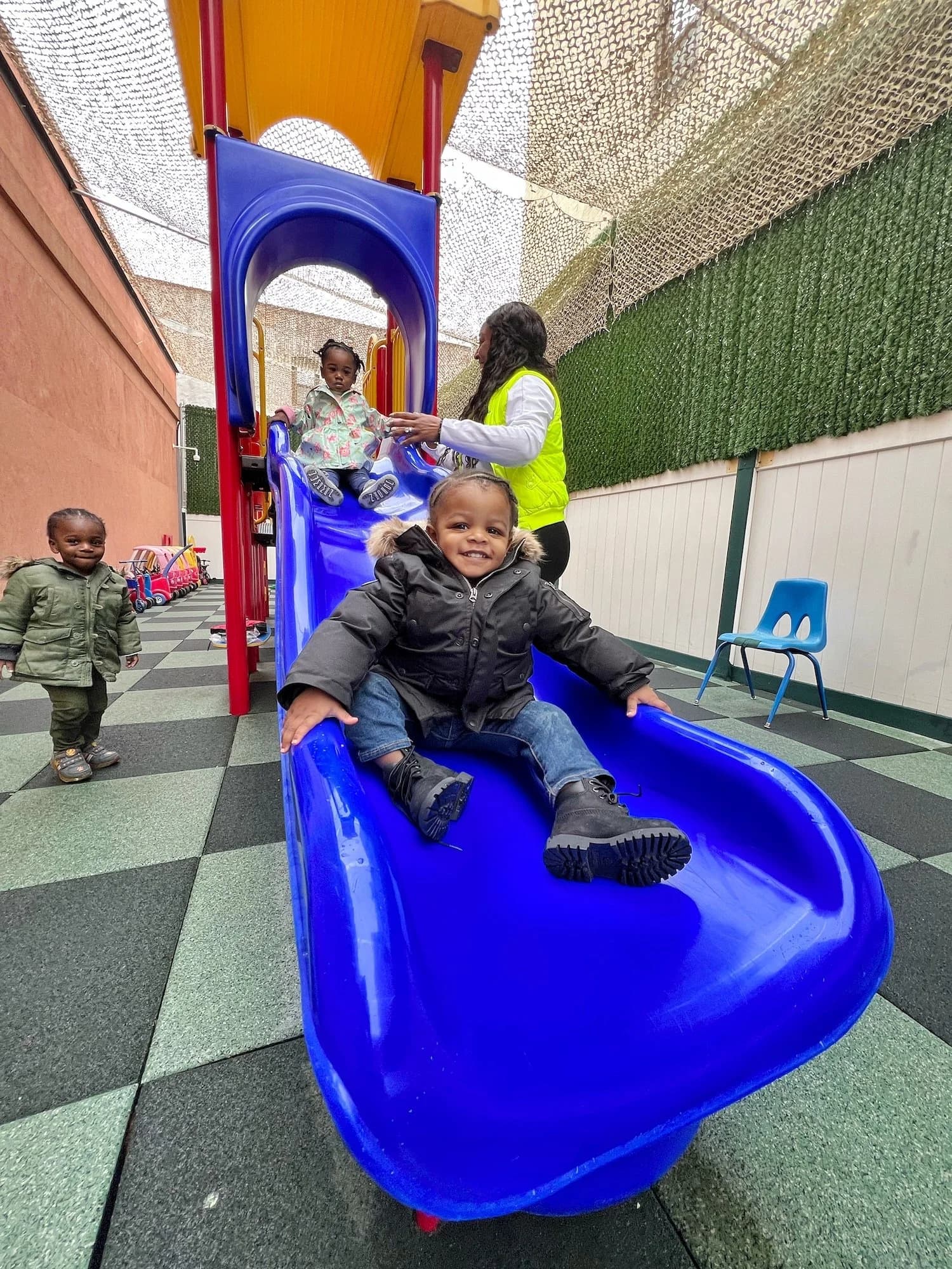 A toddler sliding down the playground slide with a staff member assisting